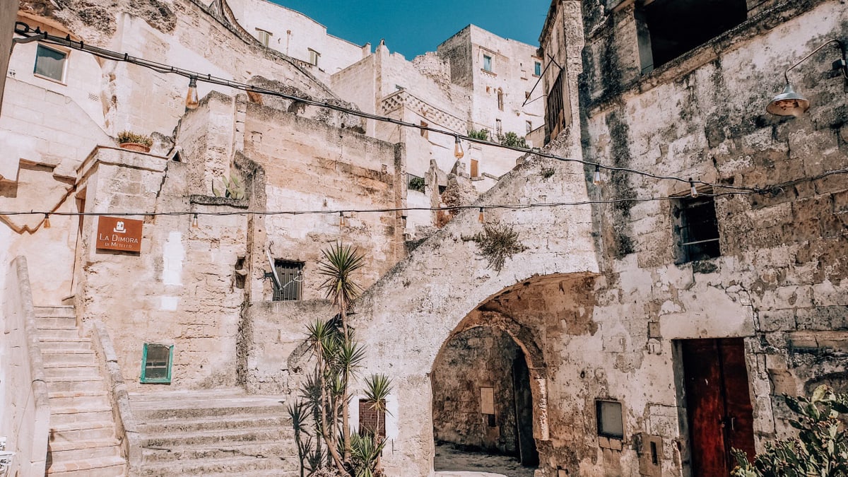Exterior of ancient city with light shabby stone walls and tropical plants in pots at bright sunlight